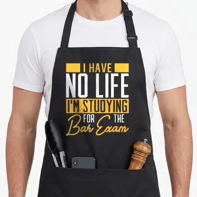 Studying bartender apron - I HAVE NO LIFE I'M STUDYING FOR THE Bar Exam text in yellow and white stacked typography — shown on a black cotton canvas apron against a white background