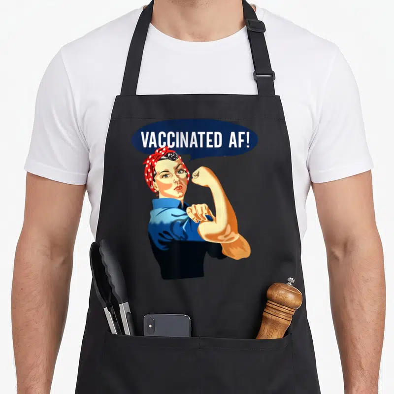 Vaccine rosie the riveter apron - VACCINATED AF! text in blue bubble above flexing woman in red headscarf — shown on a black cotton canvas apron against a white background