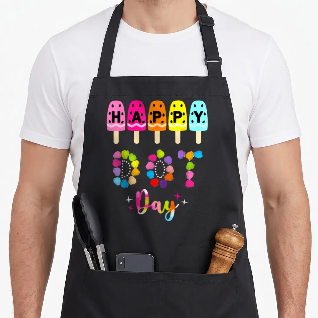 Student polka dot apron - Five popsicles pink yellow blue orange red with HAPPY DOT Day text and rainbow script — shown on a black cotton canvas apron against a white background