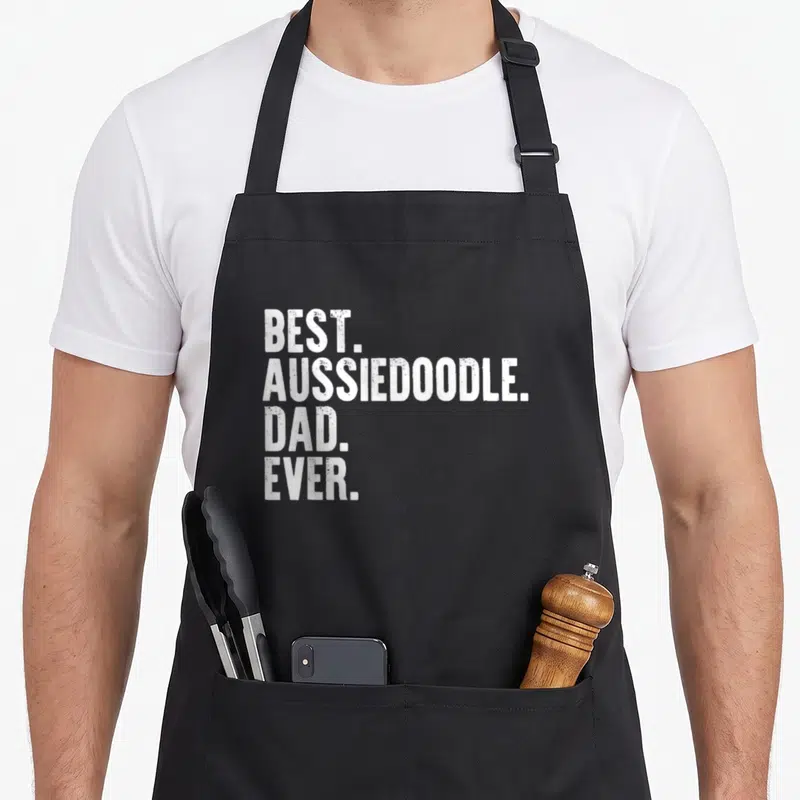 Aussiedoodle father day apron - White distressed text reading BEST. AUSSIEDOODLE. DAD. EVER. stacked in four lines — shown on a black cotton canvas apron against a white background