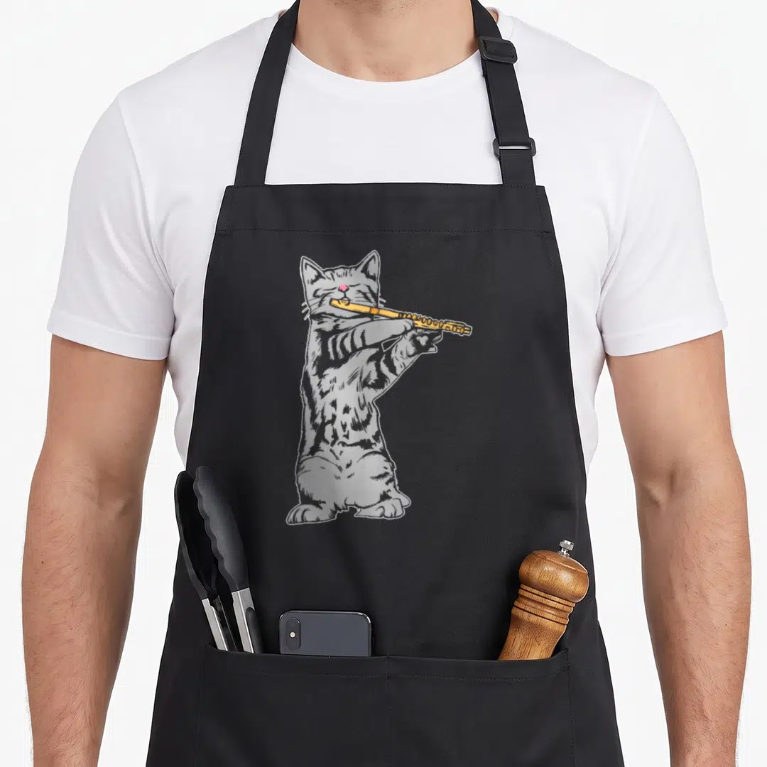 Flute cat apron - Grey cartoon cat standing on hind legs playing a yellow flute with pink nose — shown on a black cotton canvas apron against a white background