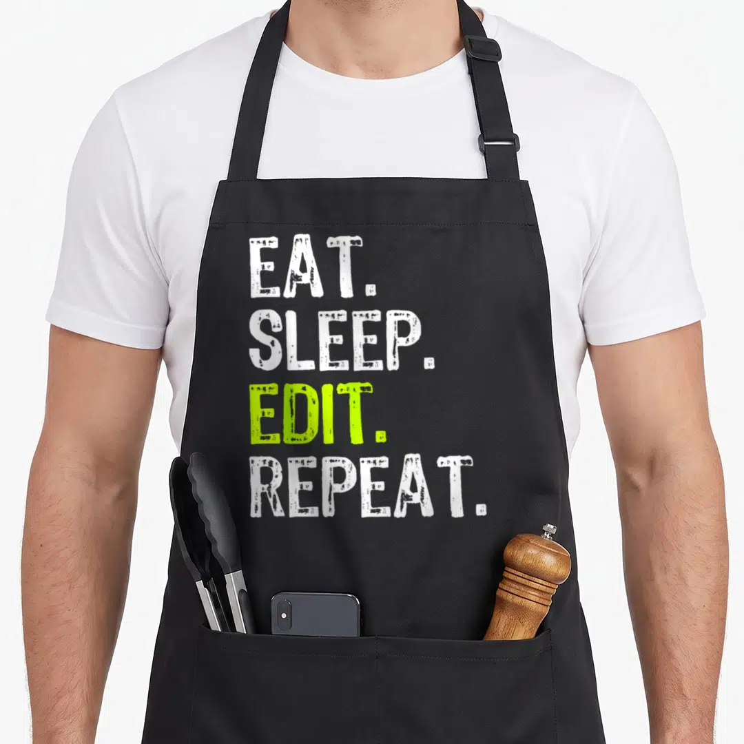 Editor edit apron - Stacked white and lime green text reading EAT SLEEP EDIT REPEAT — shown on a black cotton canvas apron against a white background