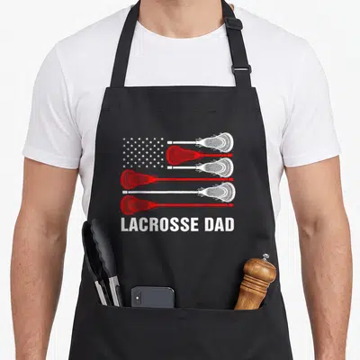 Lax lacrosse mom apron - Four red and white lacrosse sticks form stripes with stars and LACROSSE DAD text below — shown on a black cotton canvas apron against a white background