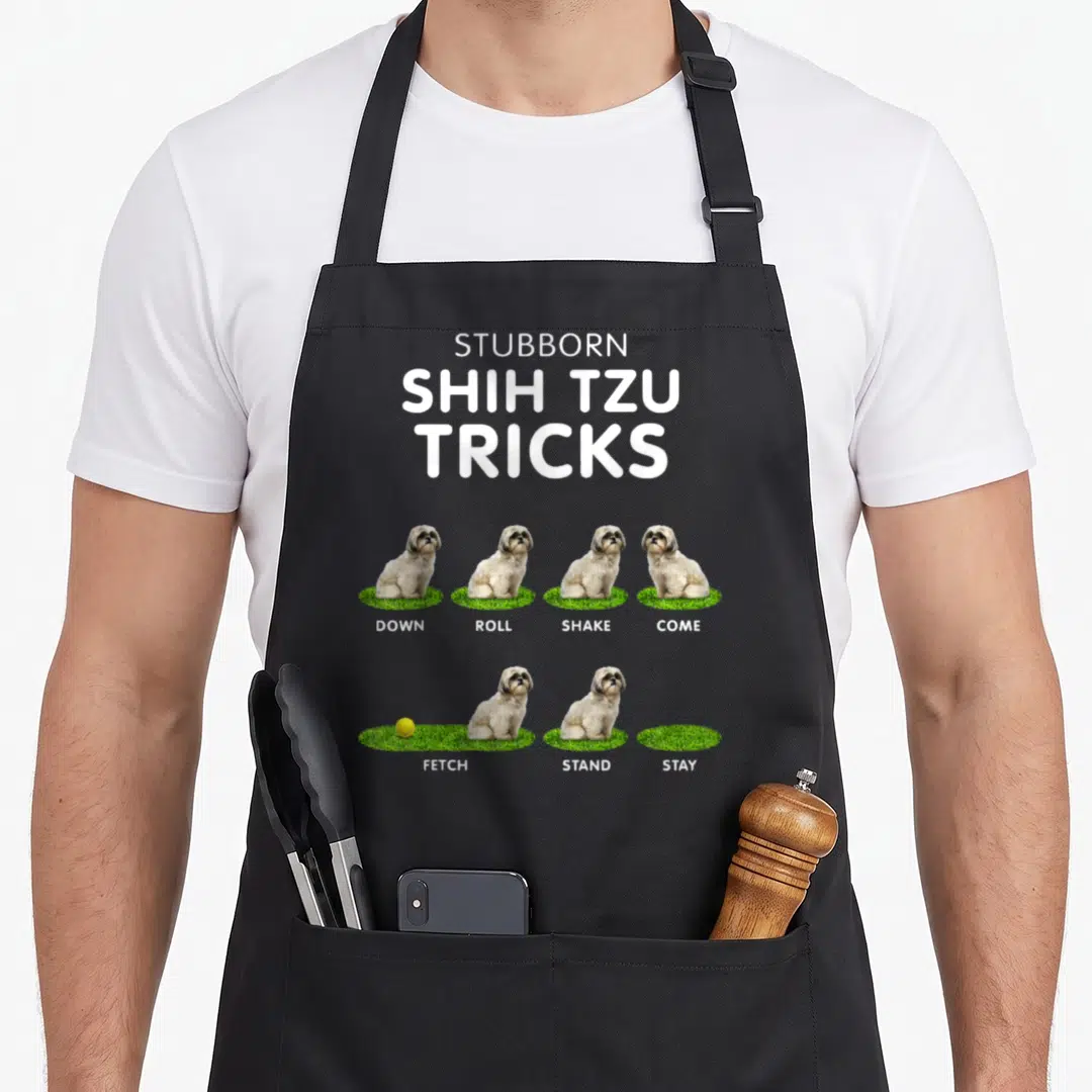 Tzu dog apron - Seven white and tan Shih Tzus sitting on green grass patches under bold white text reading Stubborn — shown on a black cotton canvas apron against a white background