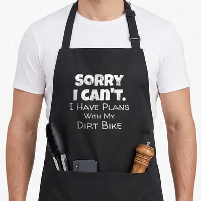 Motocross motorcycle aprons - White stacked typography reading SORRY I CAN'T I HAVE PLANS WITH MY DIRT BIKE — shown on a black cotton canvas apron against a white background