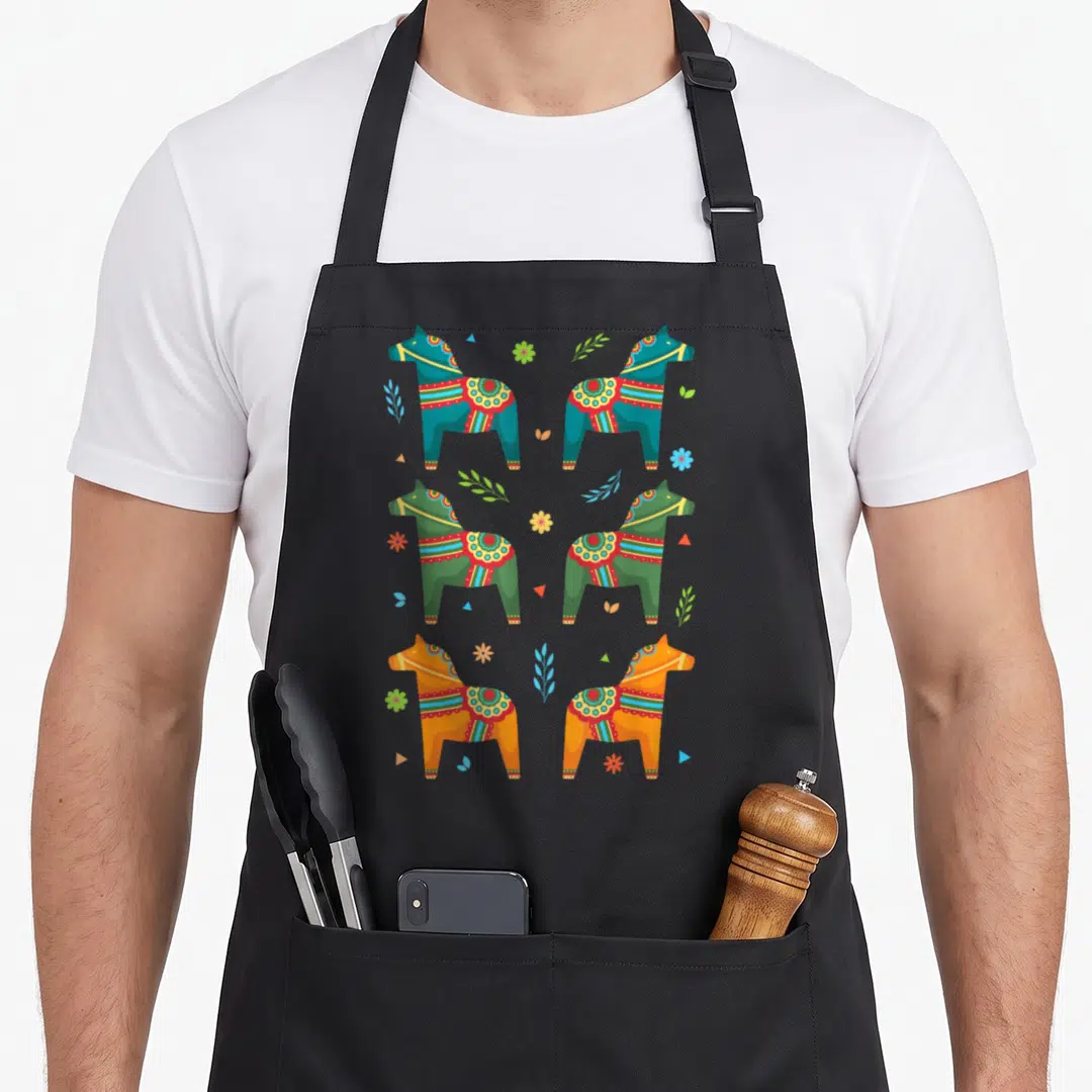 Dala scandinavian aprons - Six cartoon horses in blue, green, orange with flowers and triangles — shown on a black cotton canvas apron against a white background