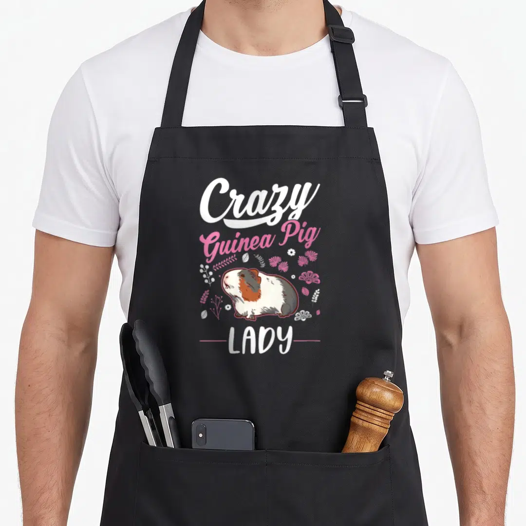 Retro animal crazy guinea lady apron - Cartoon guinea pig with white pink brown fur and floral accents — shown on a black cotton canvas apron against a white background