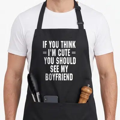Should girlfriend funny apron - White stacked text IF YOU THINK I'M CUTE YOU SHOULD SEE MY BOYFRIEND on black background — shown on a black cotton canvas apron against a white background
