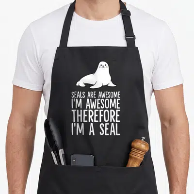 Seal awesome therefore apron - Cartoon seal above stacked text SEALS ARE AWESOME I'M AWESOME THEREFORE I'M A SEAL — shown on a black cotton canvas apron against a white background