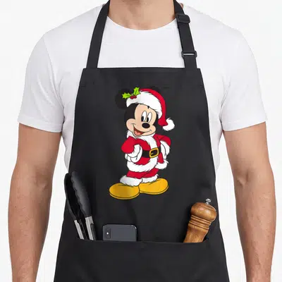 Funny holiday santa apron - Mickey Mouse in red Santa suit with holly, white trim, black belt, yellow shoes — shown on a black cotton canvas apron against a white background