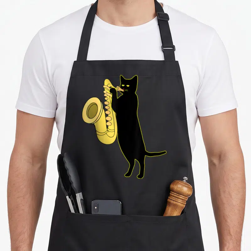 Saxophone cute cat apron - Cartoon black cat standing upright playing yellow saxophone instrument — shown on a black cotton canvas apron against a white background