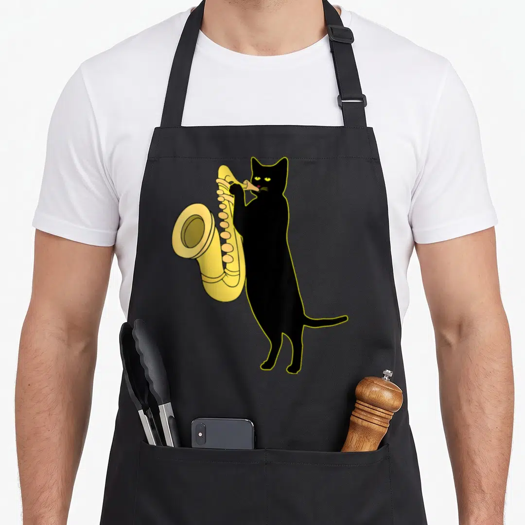 Saxophone cute cat apron - Cartoon black cat standing upright playing yellow saxophone instrument — shown on a black cotton canvas apron against a white background