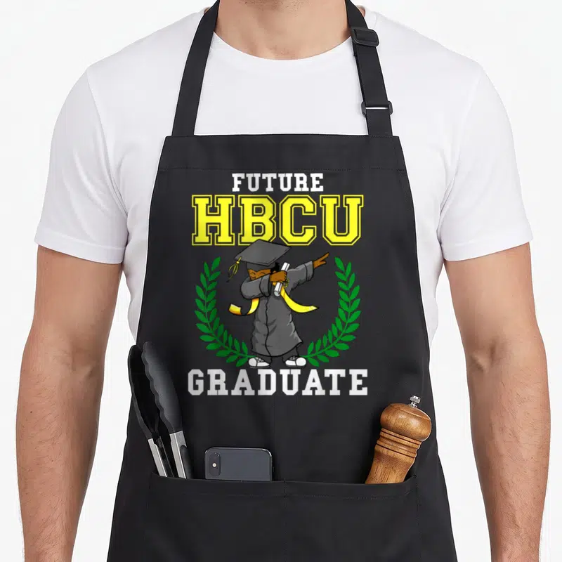Future dabbing boys apron - Cartoon graduate dabbing between FUTURE HBCU GRADUATE text and green wreath — shown on a black cotton canvas apron against a white background