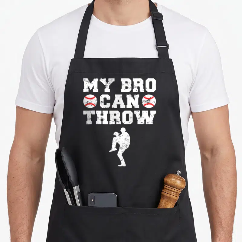 Pitcher sister baseball apron - Distressed MY BRO CAN THROW text flanked by red-stitched baseballs above a white — shown on a black cotton canvas apron against a white background