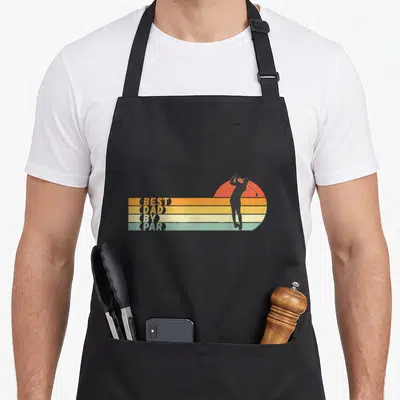 Golf par father day apron - Retro golfer silhouette over sunset circle next to stacked text BEST DAD BY PAR on colored — shown on a black cotton canvas apron against a white background