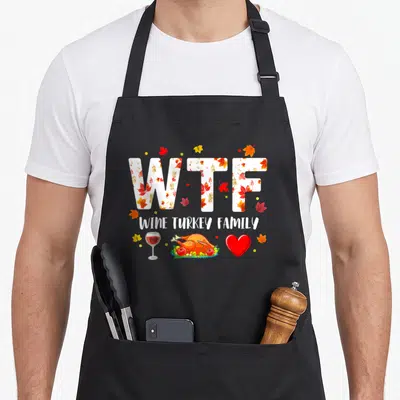 Wine turkey thanksgiving aprons - WTF WINE TURKEY FAMILY text filled with autumn leaves above a wine glass, roasted — shown on a black cotton canvas apron against a white background
