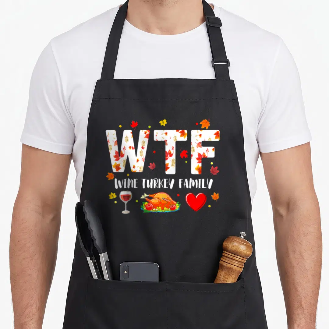 Wine turkey thanksgiving aprons - WTF WINE TURKEY FAMILY text filled with autumn leaves above a wine glass, roasted — shown on a black cotton canvas apron against a white background