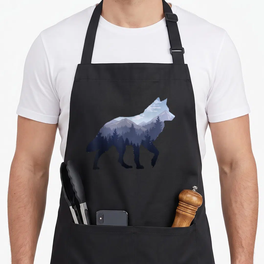 Lone mountain apron - Wolf silhouette filled with blue mountain landscape, trees, and moon in minimalist style — shown on a black cotton canvas apron against a white background