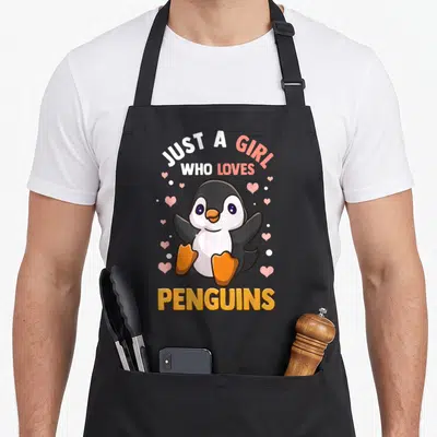 Vintage penguin aprons - Cartoon penguin with pink hearts and text Just A Girl Who Loves Penguins — shown on a black cotton canvas apron against a white background