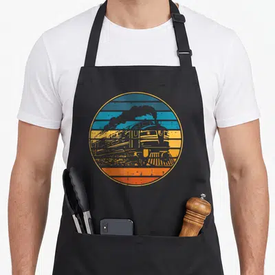 Locomotive boy train apron - Retro train silhouette against blue yellow orange and grey horizontal stripes in a circle — shown on a black cotton canvas apron against a white background