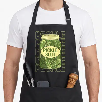 Apaprel pickle apron - Cartoon pickle jar with green pickles and yellow label reading PICKLE SLUT — shown on a black cotton canvas apron against a white background