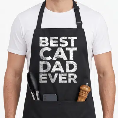 Cute father cat dad apron - White BEST CAT DAD EVER text stacked vertically on black fabric — shown on a black cotton canvas apron against a white background