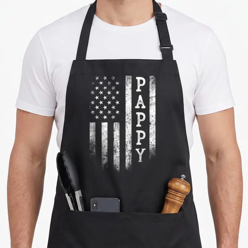 Flag patriotic father day apron - Distressed white US flag with vertical PAPPY text on black fabric — shown on a black cotton canvas apron against a white background