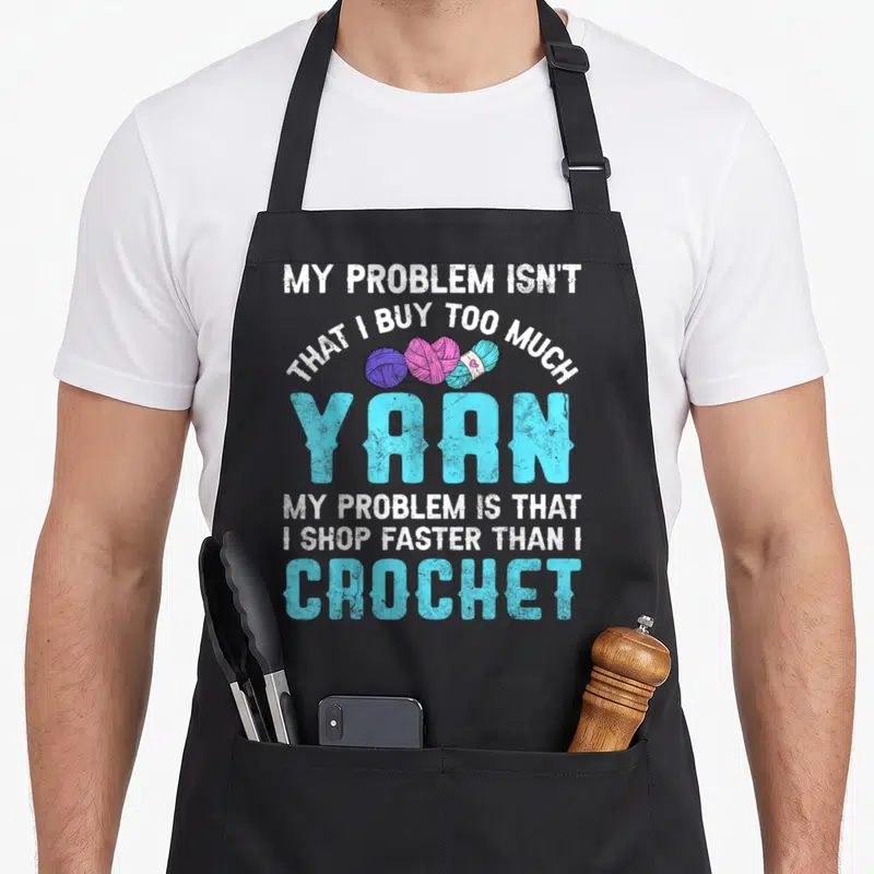 Crocheting yarn crochet apron - Distressed text reading My Problem Is Not That I Buy Too Much Yarn with purple pink — shown on a black cotton canvas apron against a white background