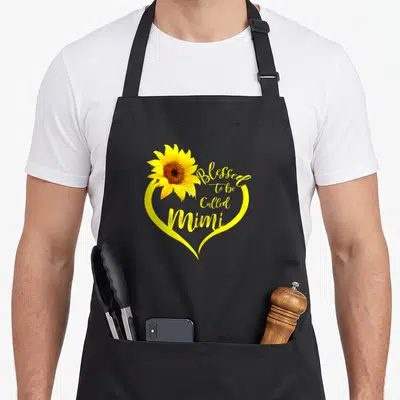 Called grandma apron - Yellow heart outline with sunflower and script text Blessed to be Called Mimi — shown on a black cotton canvas apron against a white background