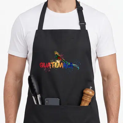 Quetzal antigua guatemala apron - Watercolor quetzal bird flying over multicolored GUATEMALA text with paint splatters — shown on a black cotton canvas apron against a white background