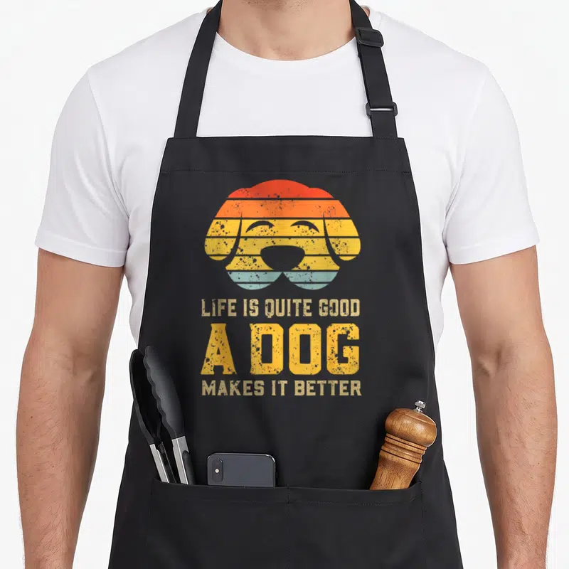 Quite dog apron - Retro striped dog head with red orange yellow blue bands and stacked text LIFE IS QUITE GOOD A DOG — shown on a black cotton canvas apron against a white background