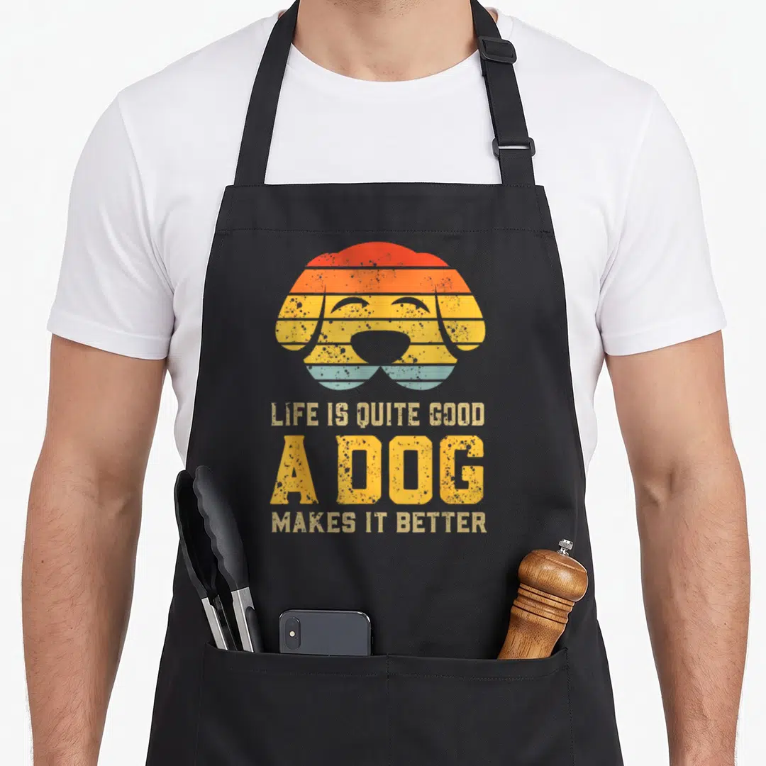 Quite dog apron - Retro striped dog head with red orange yellow blue bands and stacked text LIFE IS QUITE GOOD A DOG — shown on a black cotton canvas apron against a white background