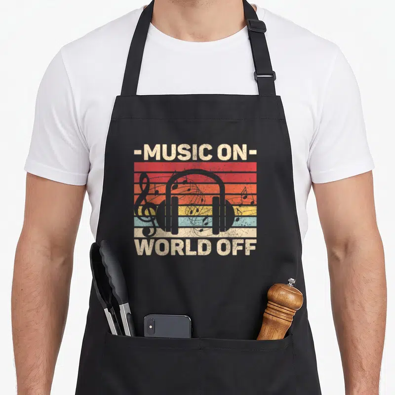 Outfit music apron - Retro graphic of grey headphones and notes over red orange yellow blue beige stripes with text — shown on a black cotton canvas apron against a white background