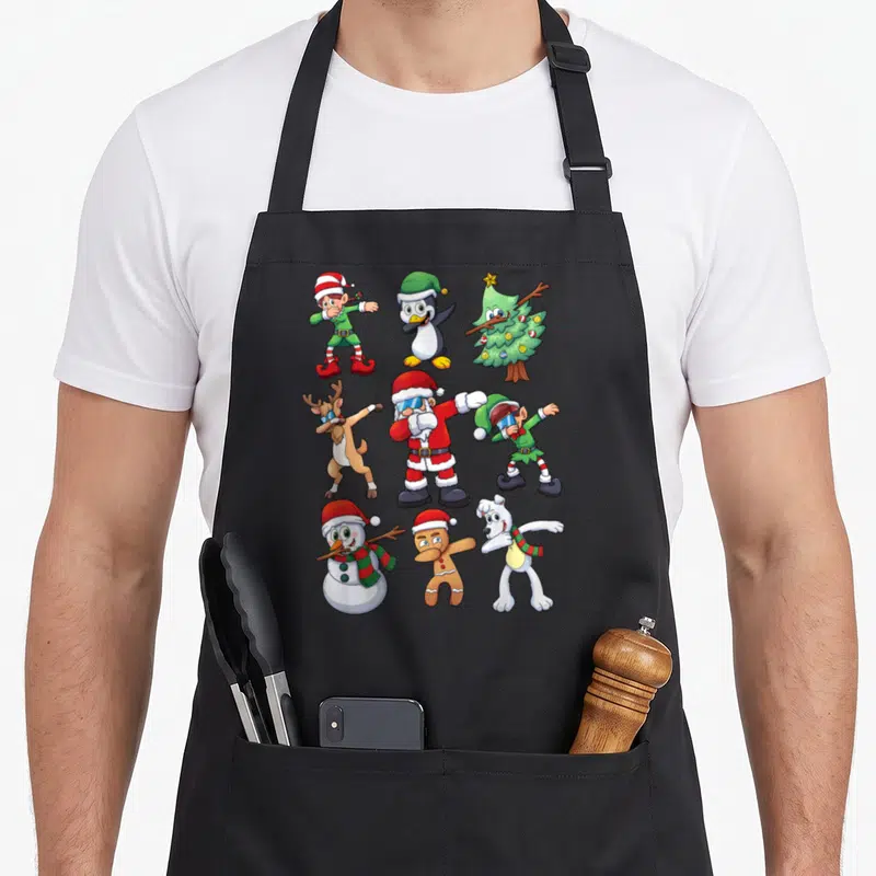 Dabbing christmas santa apron - Nine cartoon Christmas characters including Santa and reindeer dabbing in a grid pattern — shown on a black cotton canvas apron against a white background