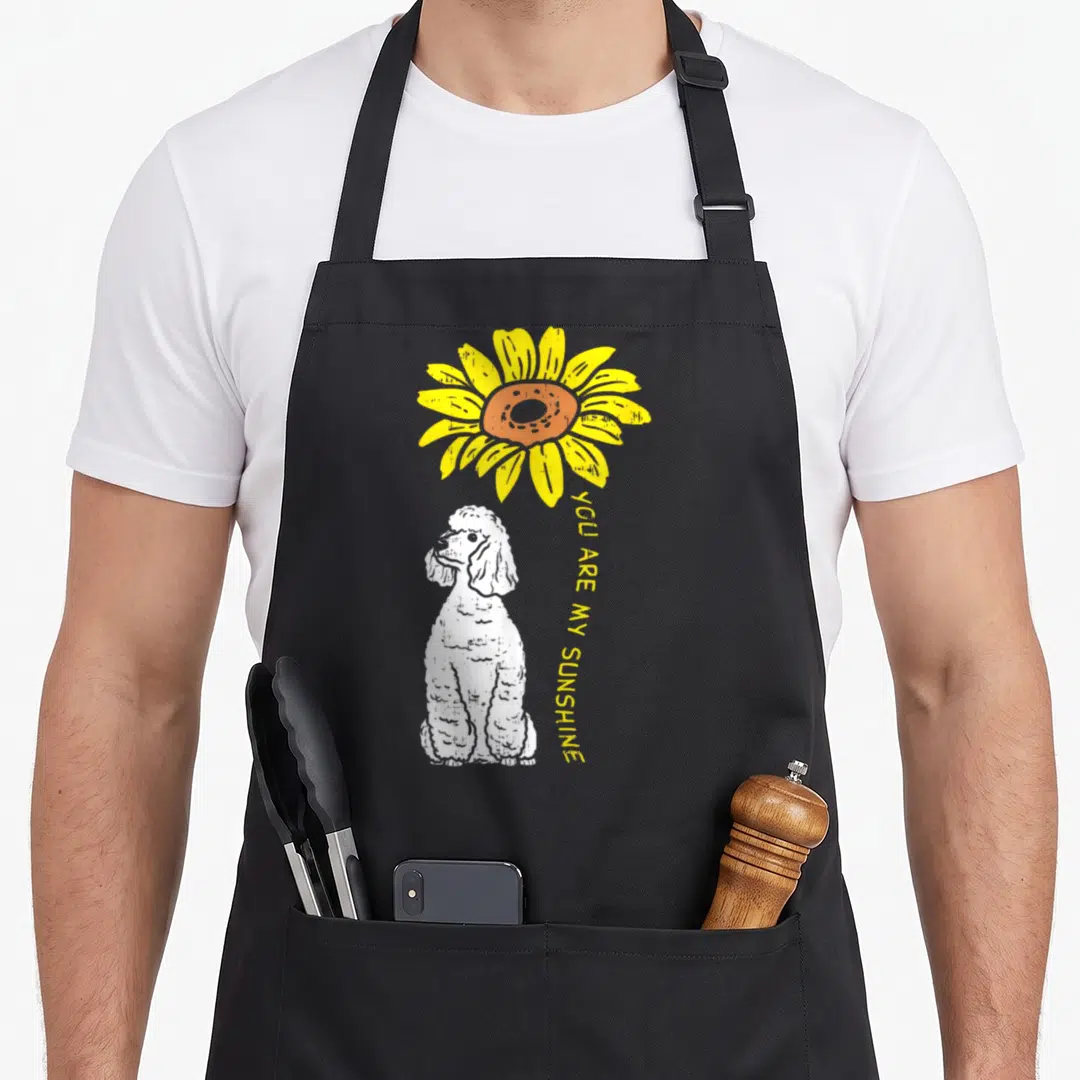 Sunflower sunshine dog apron - White poodle sitting below yellow sunflower with vertical YOU ARE MY SUNSHINE text — shown on a black cotton canvas apron against a white background