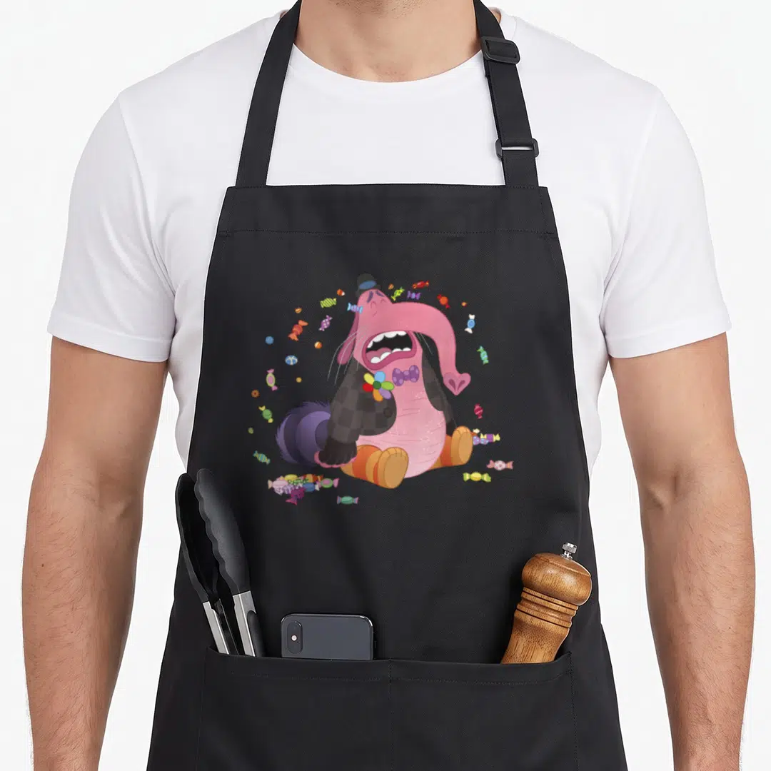 Bing cotton candy apron - Crying pink elephant cartoon seated among scattered colorful wrapped candies — shown on a black cotton canvas apron against a white background