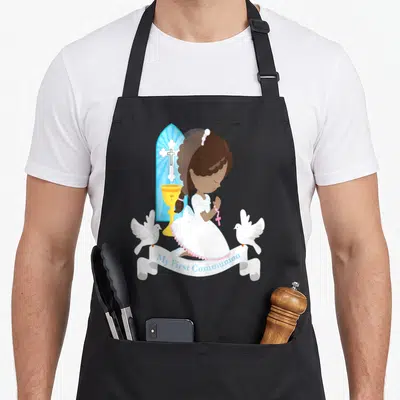 African communion aprons - Cartoon girl kneeling in prayer with doves chalice and My First Communion ribbon — shown on a black cotton canvas apron against a white background