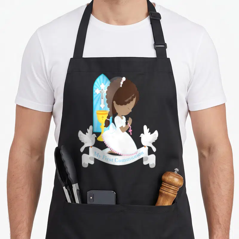 African communion aprons - Cartoon girl kneeling in prayer with doves chalice and My First Communion ribbon — shown on a black cotton canvas apron against a white background