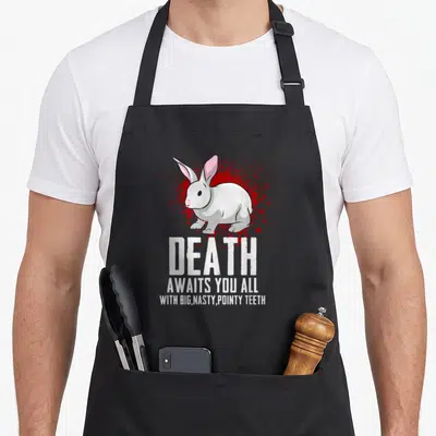 Death rabbit apron - White rabbit on red splatter with text DEATH AWAITS YOU ALL WITH BIG NASTY POINTY TEETH — shown on a black cotton canvas apron against a white background