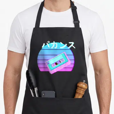 Tape 90s apron - Tilted pink cassette tape over blue magenta striped sun with white Japanese katakana text — shown on a black cotton canvas apron against a white background