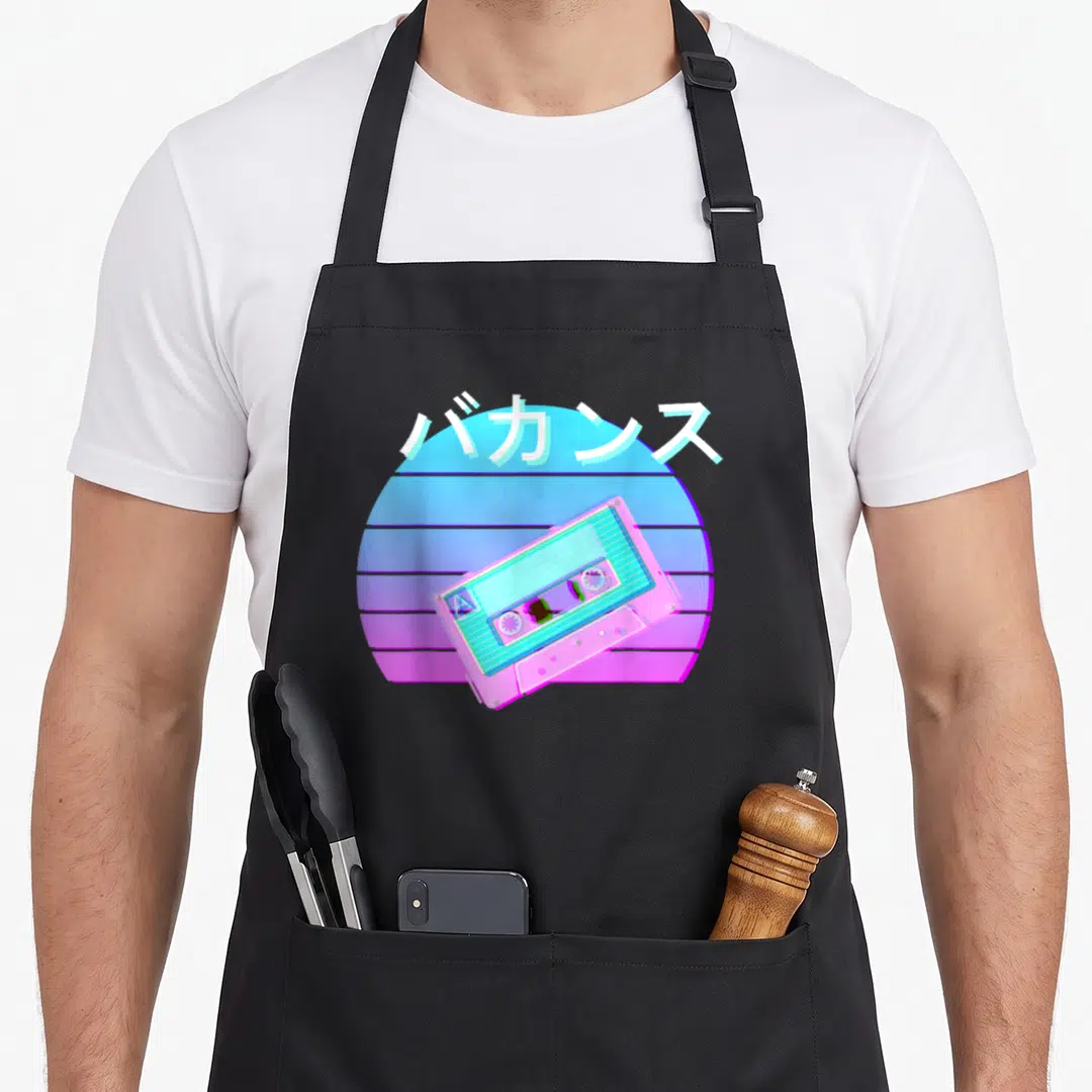 Tape 90s apron - Tilted pink cassette tape over blue magenta striped sun with white Japanese katakana text — shown on a black cotton canvas apron against a white background