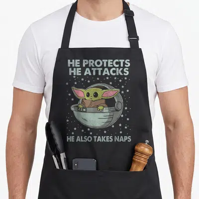 Nap may look apron - He Protects He Attacks He Also Takes Naps text surrounding green character in grey pod with stars — shown on a black cotton canvas apron against a white background