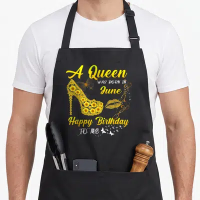 June sunflower apron - A Queen WAS BORN IN June Happy Birthday TO ME text with sunflower high heel shoe and lips — shown on a black cotton canvas apron against a white background