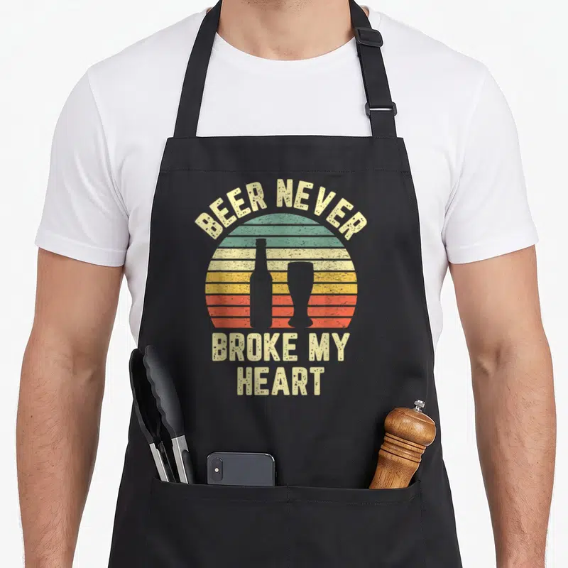 Broke drinking beer apron - Retro striped sunset with beer bottle silhouette and text BEER NEVER BROKE MY HEART — shown on a black cotton canvas apron against a white background