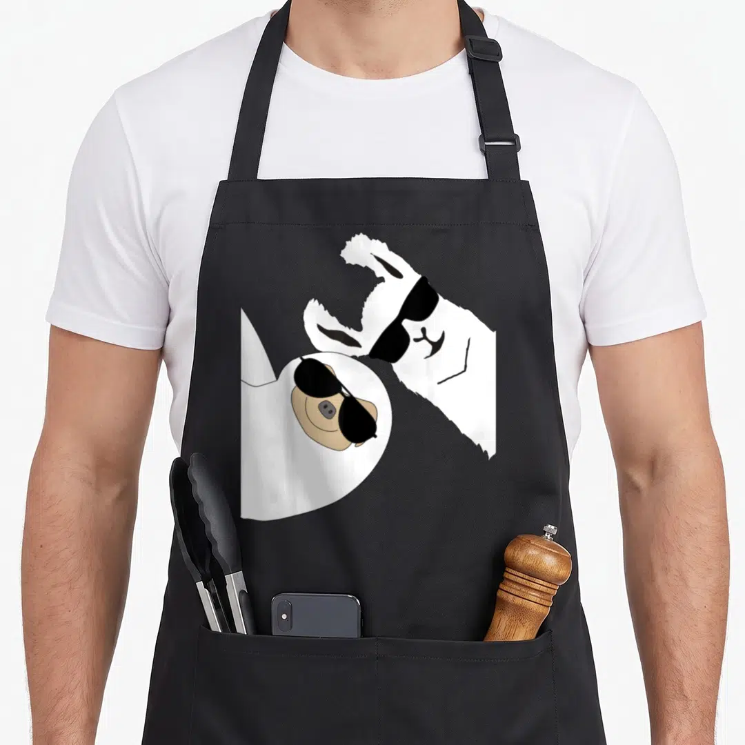 Sloth alpaca apron - Cartoon llama and tan pig in white sheet wearing black sunglasses — shown on a black cotton canvas apron against a white background