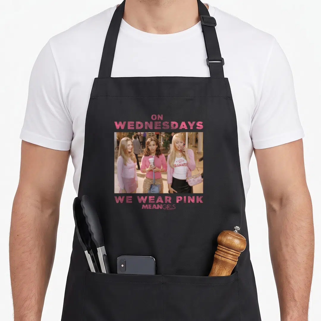 Wednesday novelty apron - Three women in pink with text On Wednesdays We Wear Pink Mean Girls — shown on a black cotton canvas apron against a white background