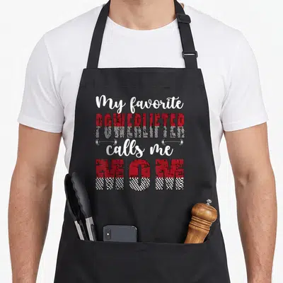 Powerlifter powerlifting apron - Stacked text "My favorite POWERLIFTER calls me MOM" with two silver dumbbells between — shown on a black cotton canvas apron against a white background