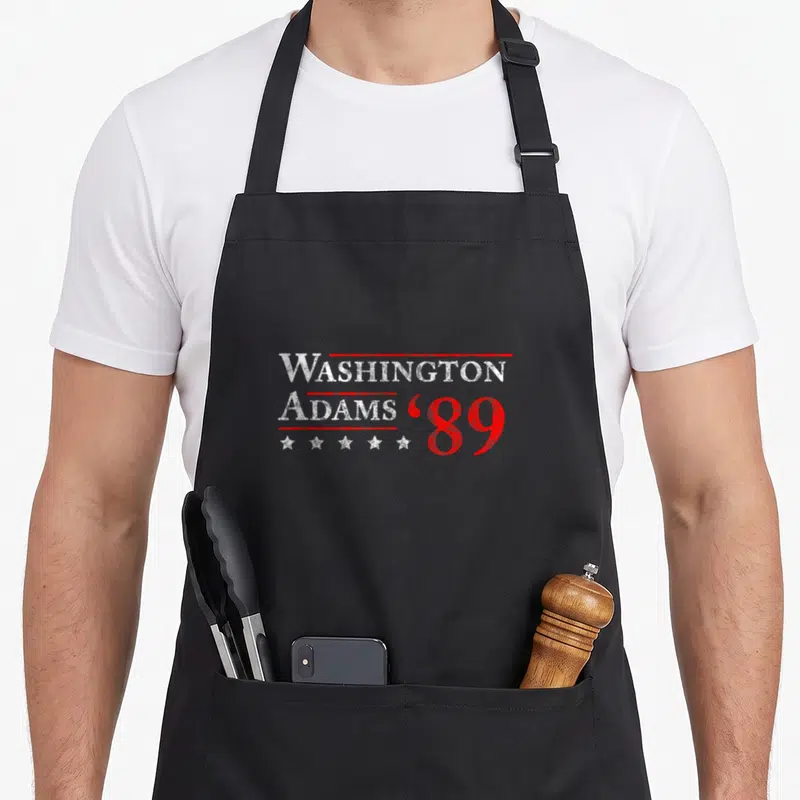 Adam 4th of july apron - Stacked WASHINGTON ADAMS text with red lines, five white stars, and red '89 in distressed style — shown on a black cotton canvas apron against a white background