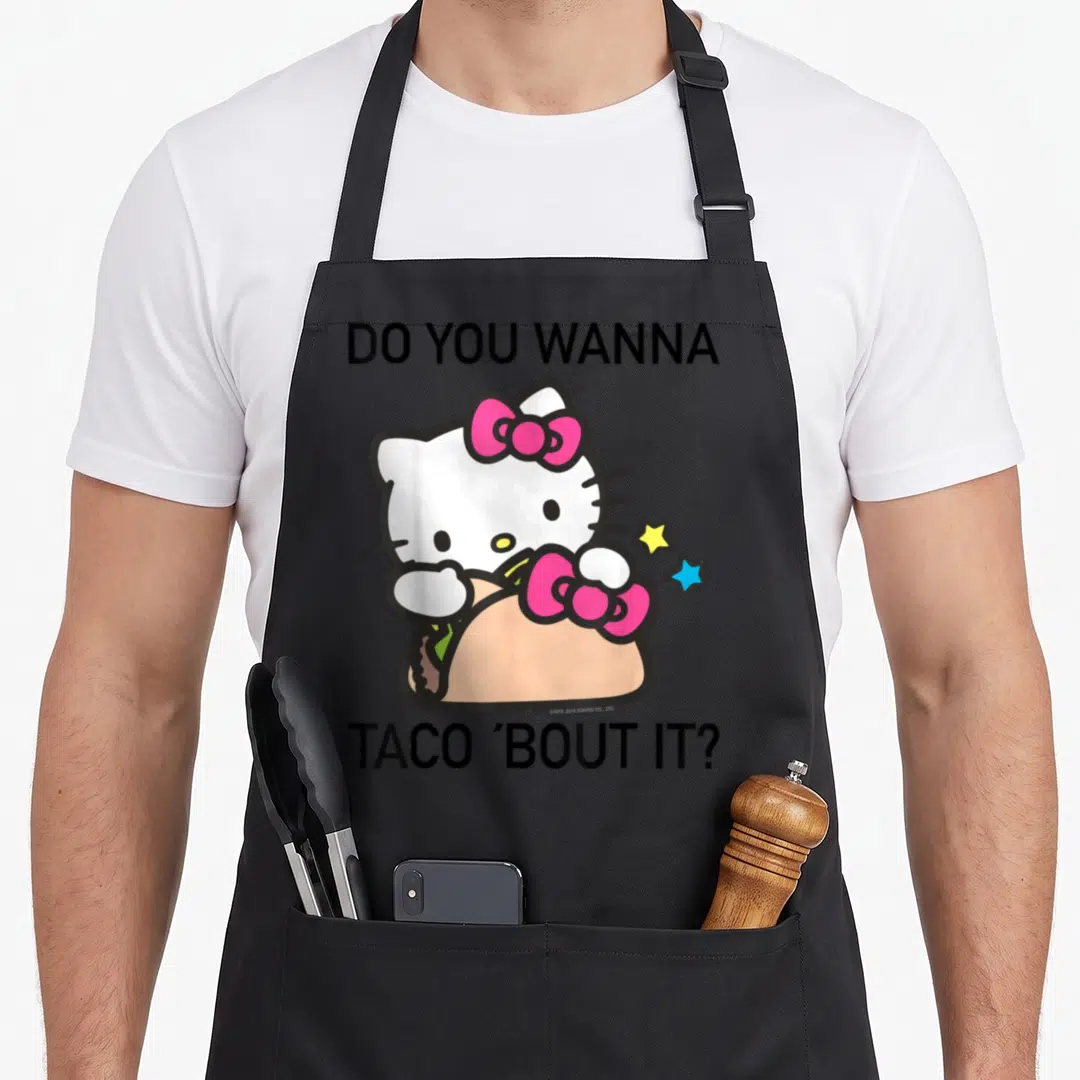 Bout taco apron - Hello Kitty in tan taco with DO YOU WANNA TACO 'BOUT IT? text and two stars — shown on a black cotton canvas apron against a white background