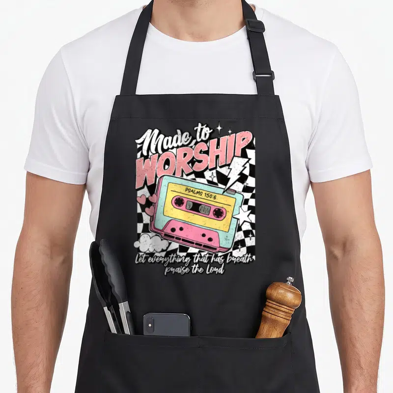 Cassette christian apron - Retro cassette tape with Made to Worship text and Psalms 150:6 on checkerboard background — shown on a black cotton canvas apron against a white background